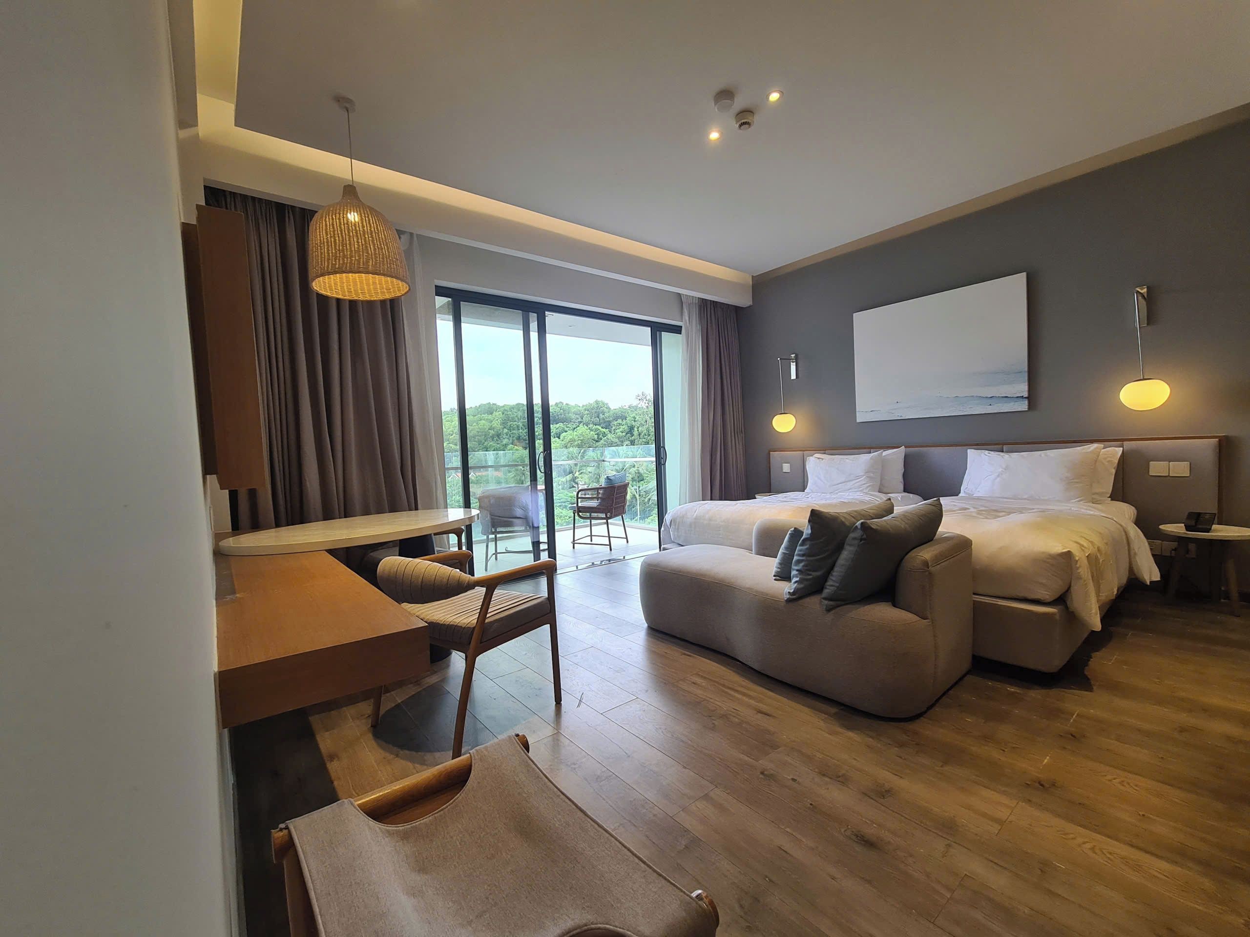 A modern hotel room with a large bed, a sofa, a desk, and a balcony with a view.