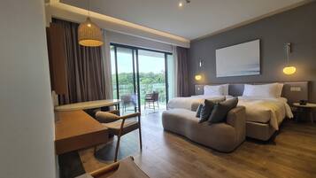 A modern hotel room with a large bed, a sofa, a desk, and a balcony with a view.
