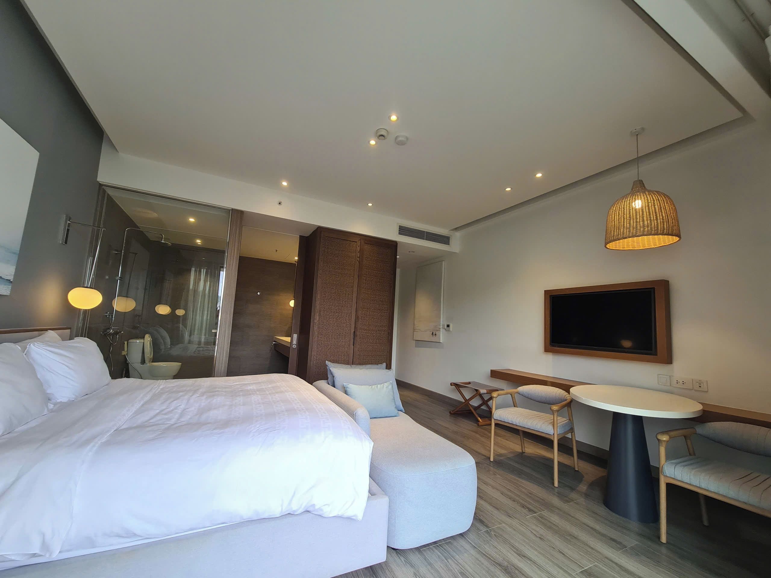 A modern hotel room with a large bed, a seating area with a table, and a television.