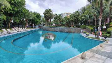 Piscina com espreguiçadeiras, palmeiras e um muro de pedra.