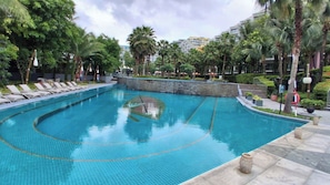Una piscina con sillas de descanso, palmeras y un muro de piedra.