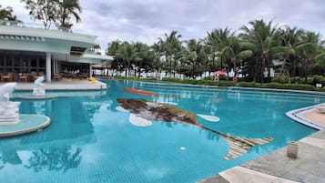 Piscina com escultura de golfinho, palmeiras e um edifício com área de estar ao ar livre.