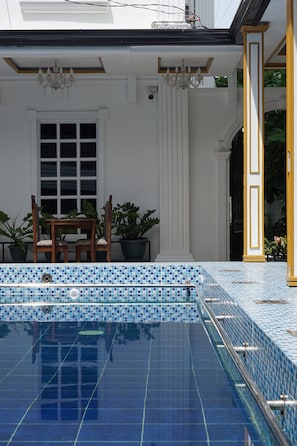 A swimming pool with blue mosaic tiles, a wooden chair, and potted plants. - San Franz Hotel La Perla (San Francisco)
