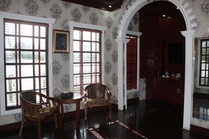 A room with two wooden chairs, a table, and a large window with blinds.