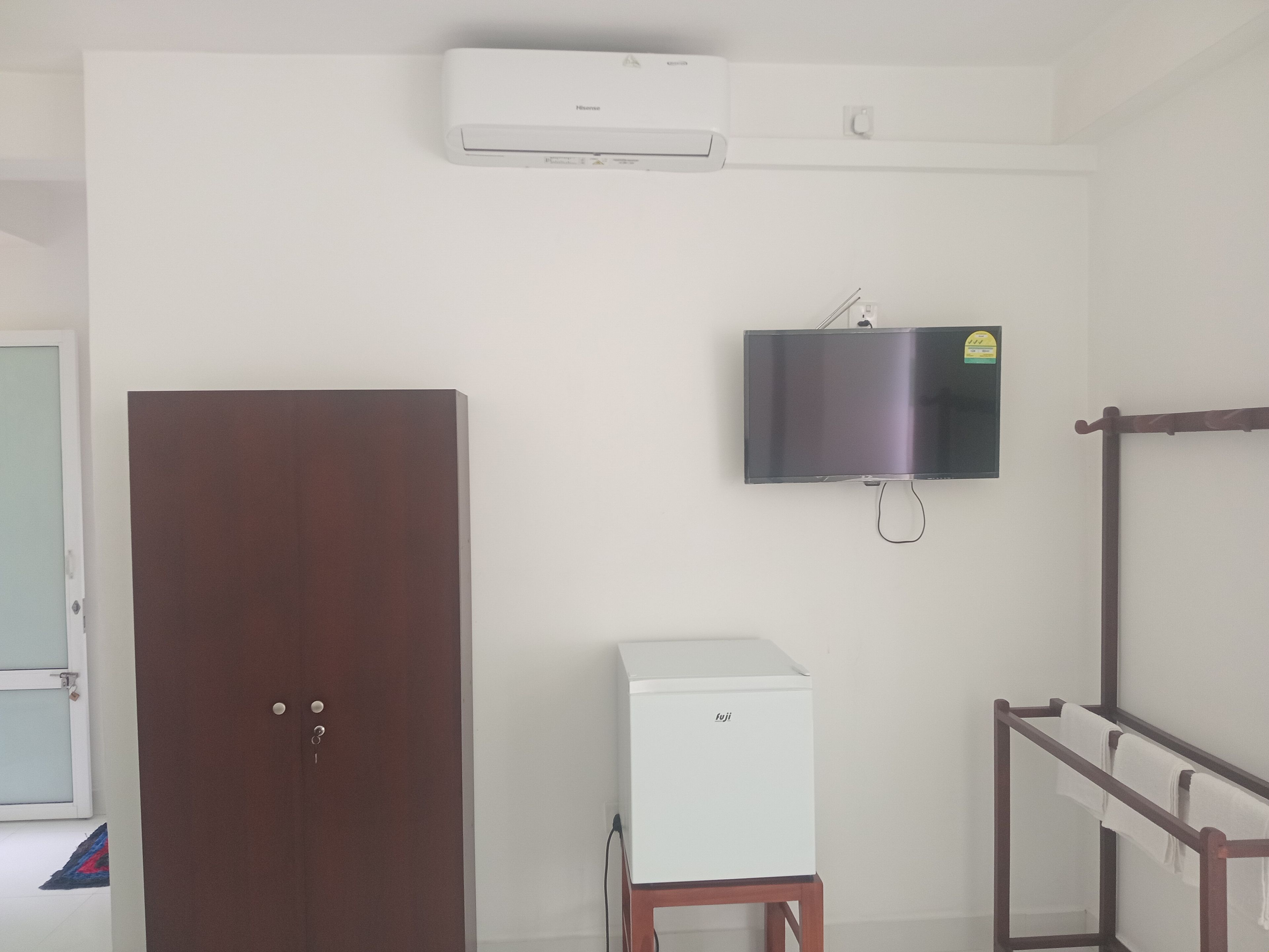 A room with a wardrobe, a small white appliance, a mounted television, and a towel rack.
