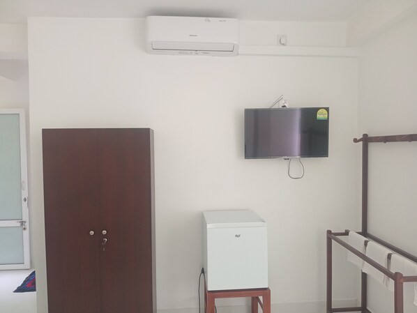 Una habitación con armario, un electrodoméstico pequeño blanco, televisor montado y un perchero.