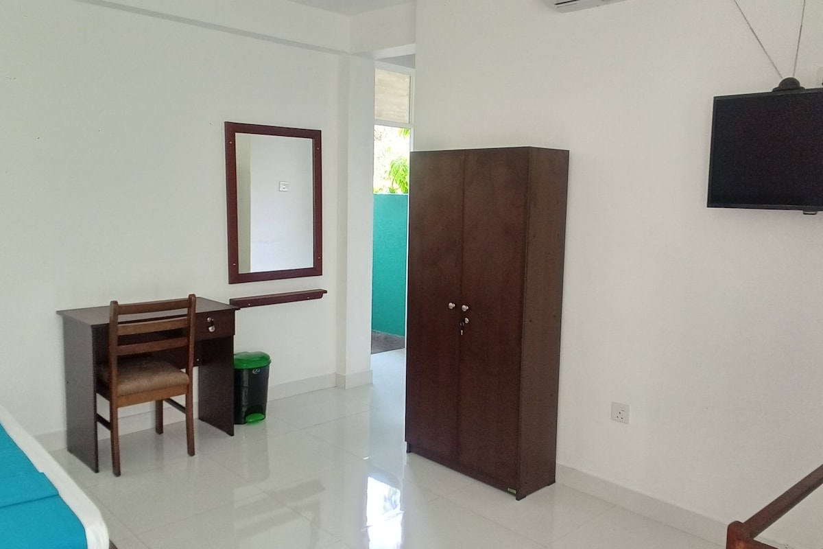 Una habitación con cama, escritorio, armario, espejo y televisor.