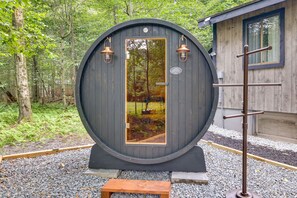 A rustic wooden structure with a round door, a small bench, and a metal rack. - Poconos Cabin w/ Sauna! Lakes ~ Skiing ~ Fire Pit (Big Bass Lake)