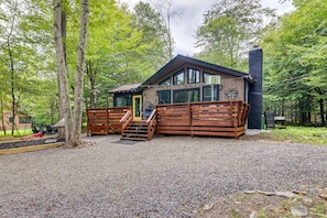 Une cabane dotée d’une terrasse en bois, d’un espace salon couvert et d’une allée gravillonnée.