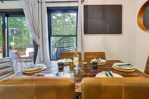 Ein Essbereich mit einem Holztisch, gedeckt für vier Personen, umgeben von Ledersesseln und Blick auf Grün durch das Fenster.