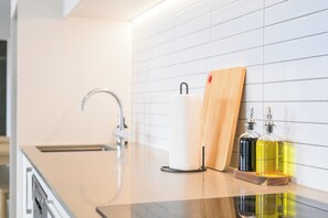 Une cuisine au design moderne, dotée d’un évier en acier inoxydable, d’une planche à découper en bois et de deux bouteilles en verre contenant de l’huile.