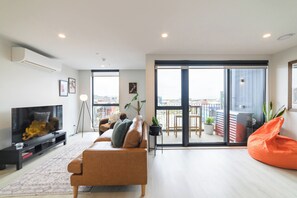 A modern living room with a sofa, a TV, and a balcony with a view. - 2BR with Balcony in Christchurch CBD - Sleeps 4 (Christchurch)