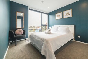 A hotel room with a large bed, a chair, a window with a view, and two framed pictures on the wall. - 2BR with Balcony in Christchurch CBD - Sleeps 4 (Christchurch)
