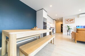 A modern living room with a wooden dining table and bench, a sofa, and a small side table with a plant. - 2BR with Balcony in Christchurch CBD - Sleeps 4 (Christchurch)