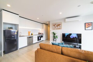 A modern kitchen with white cabinets, a black refrigerator, and a dining area with a brown sofa and a flat-screen TV. - 2BR with Balcony in Christchurch CBD - Sleeps 4 (Christchurch)
