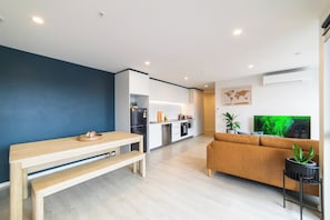 A modern living room with a wooden bench, a sofa, and a television. - 2BR with Balcony in Christchurch CBD - Sleeps 4 (Christchurch)
