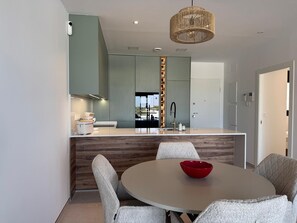 A modern kitchen with a central island, a dining area with a round table and chairs, and a hanging light fixture. - Luxury Golf View | Pool | EV Charger | Near the Beach (Los Alcázares)