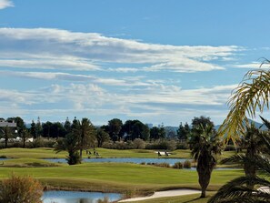 A golf course with water hazards, palm trees, and a clear sky. - Luxury Golf View | Pool | EV Charger | Near the Beach (Los Alcázares)