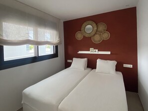 A bedroom with two beds, a window with sheer curtains, a wall-mounted mirror, and a shelf with decorative items. - Luxury Golf View | Pool | EV Charger | Near the Beach (Los Alcázares)