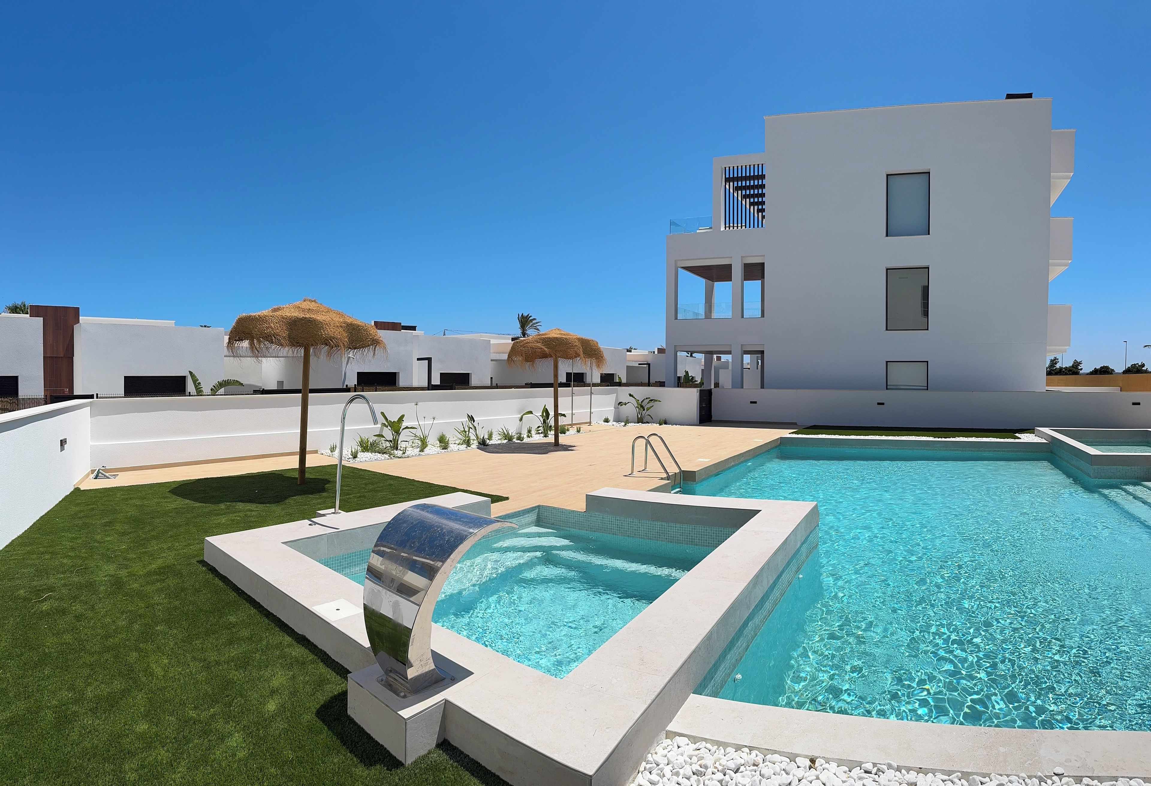 Un espace piscine moderne avec une piscine à l’eau d’un bleu limpide, une chaise longue et un parasol en chaume.