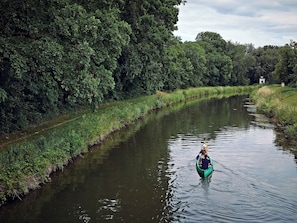 A narrow waterway flanked by dense greenery, with a small structure in the distance.