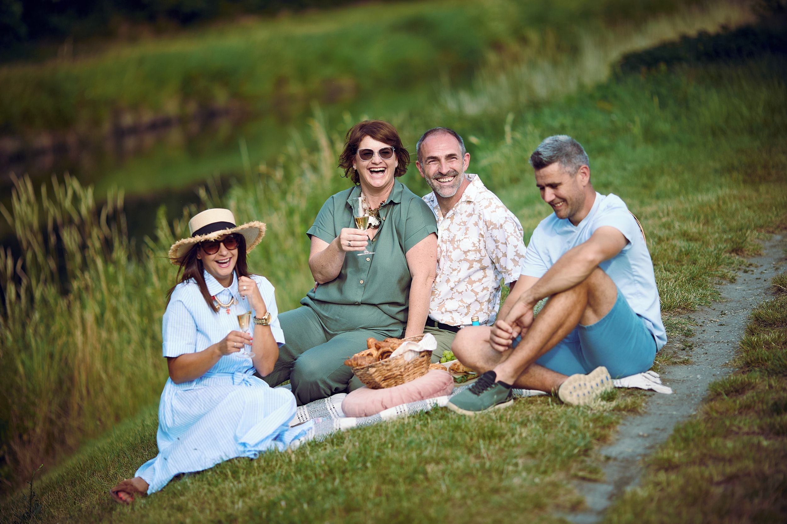 A group of people sitting on grass by a path in a natural setting.