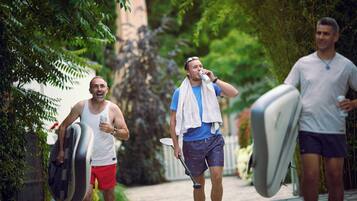 Tres personas caminando por un sendero con tablas de surf, una sosteniendo una lata y otra con una toalla al cuello.