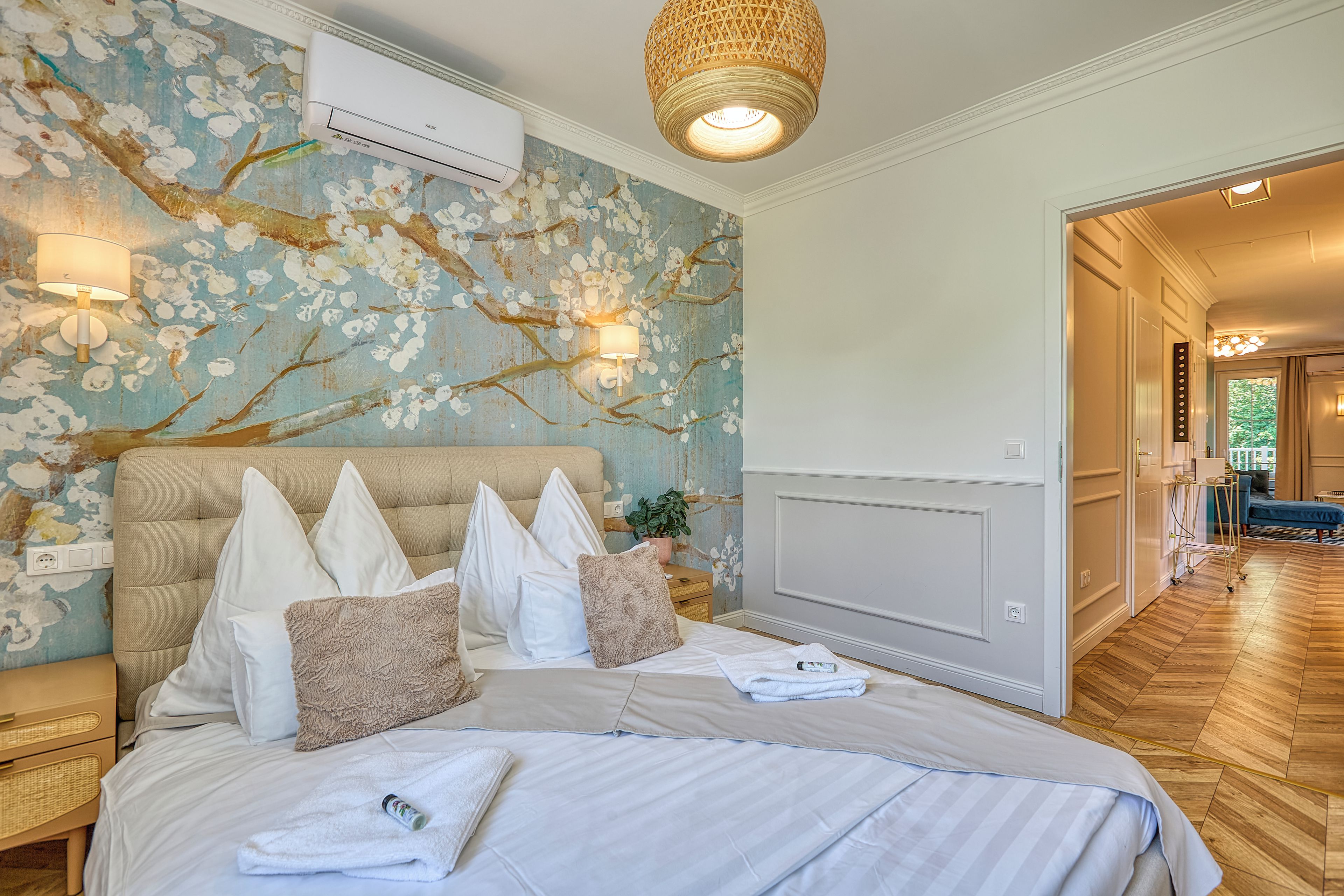 A bedroom with a bed, pillows, a wall-mounted air conditioner, a lamp, and a plant.
