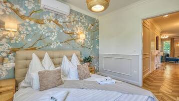 A bedroom with a bed, pillows, a wall-mounted air conditioner, a lamp, and a plant.