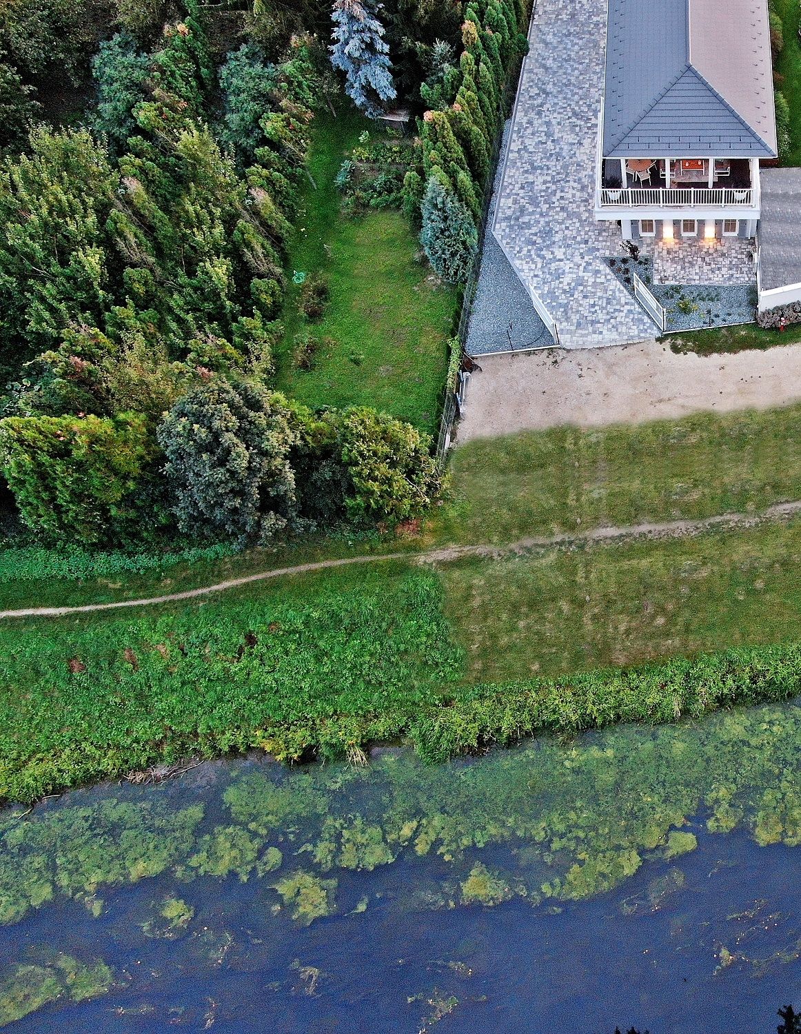 Vista aérea de una casa con techo inclinado, rodeada de un césped cuidado y árboles frondosos.