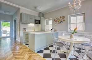A modern kitchen with a central island, clear chairs, and a dining table. - The Doors Apartments (Mosonmagyaróvár)