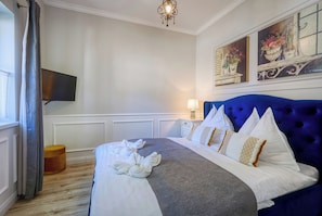 A hotel room with a large bed, a flat-screen TV mounted on the wall, and artwork above the bed.