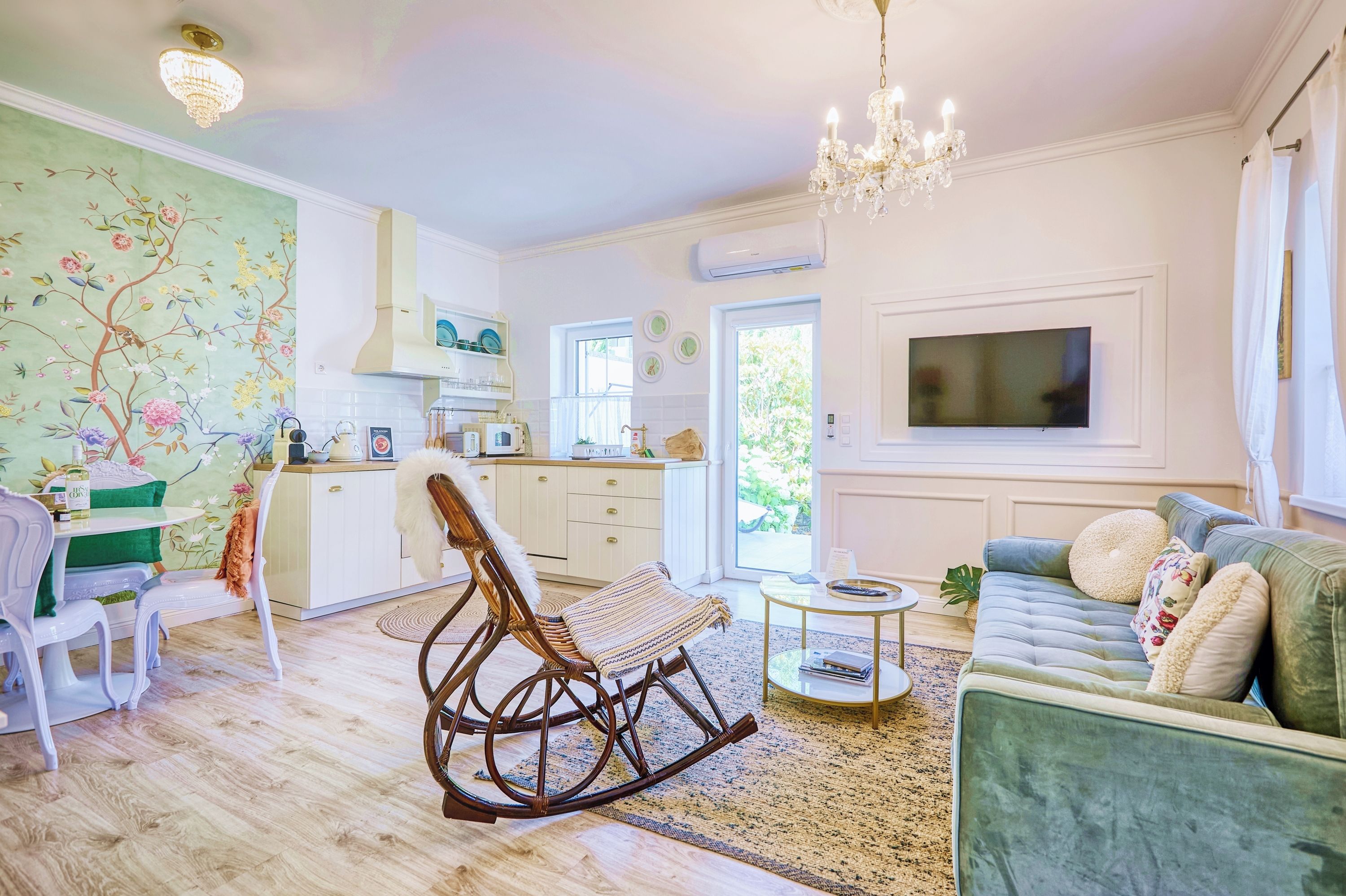 A living room with a sofa, a rocking chair, a television, and a kitchen area with a dining table.