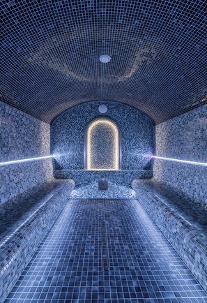 Un spa moderno con suelo y paredes alicatadas, un ventanal arqueado central y una zona de estar.