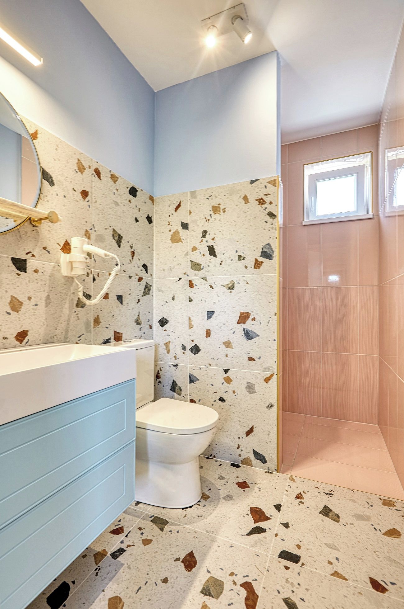 A bathroom with a white toilet, a blue vanity, and a shower area with a window.