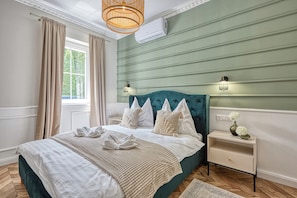 A bedroom with a large bed, a bedside table, a nightstand, a window with curtains, and a hanging light fixture.