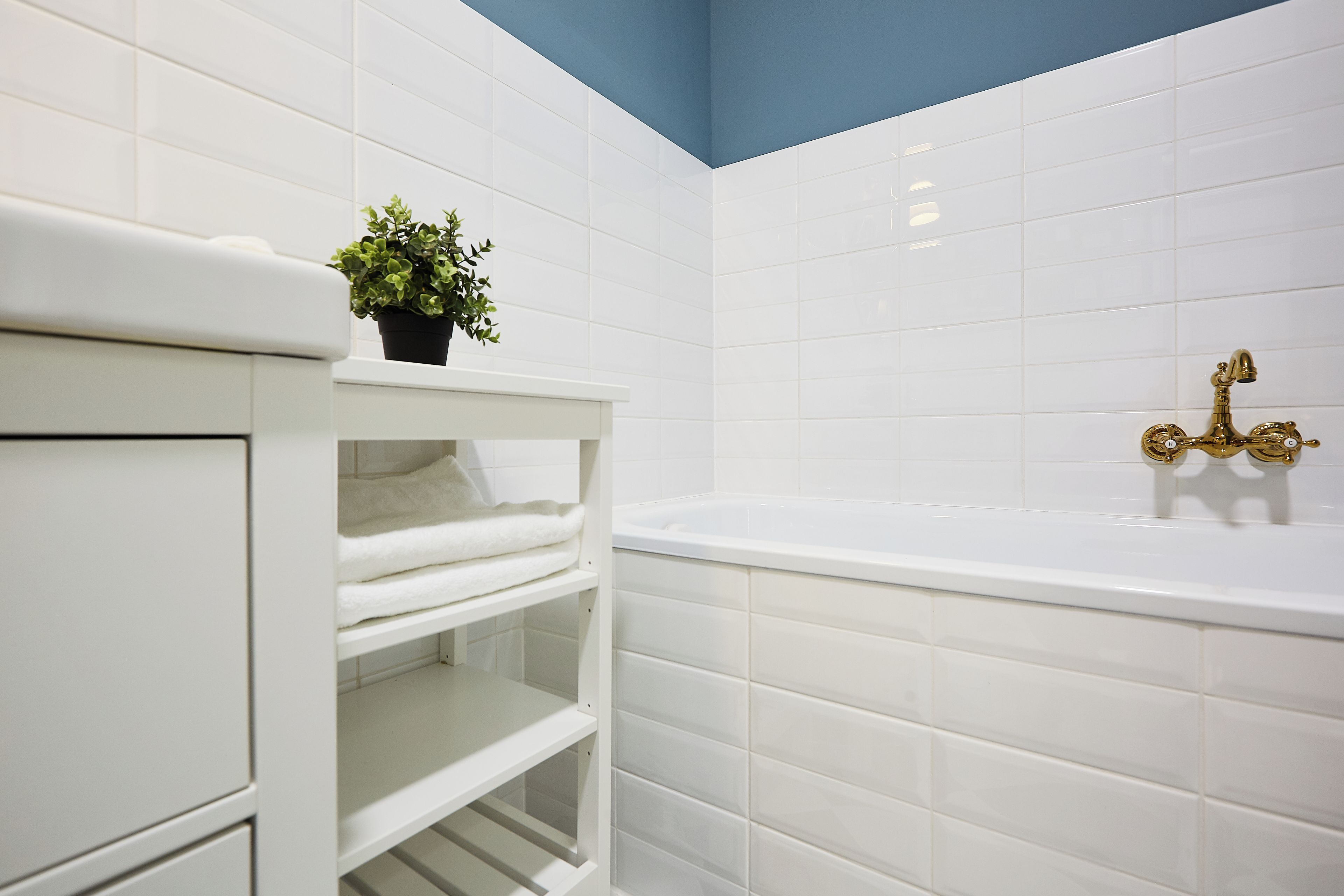A bathroom with white tiled walls, a white vanity with a plant on top, and a gold-colored bathtub.