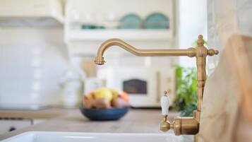 A kitchen sink with a brass faucet and a bowl of fruit in the background.