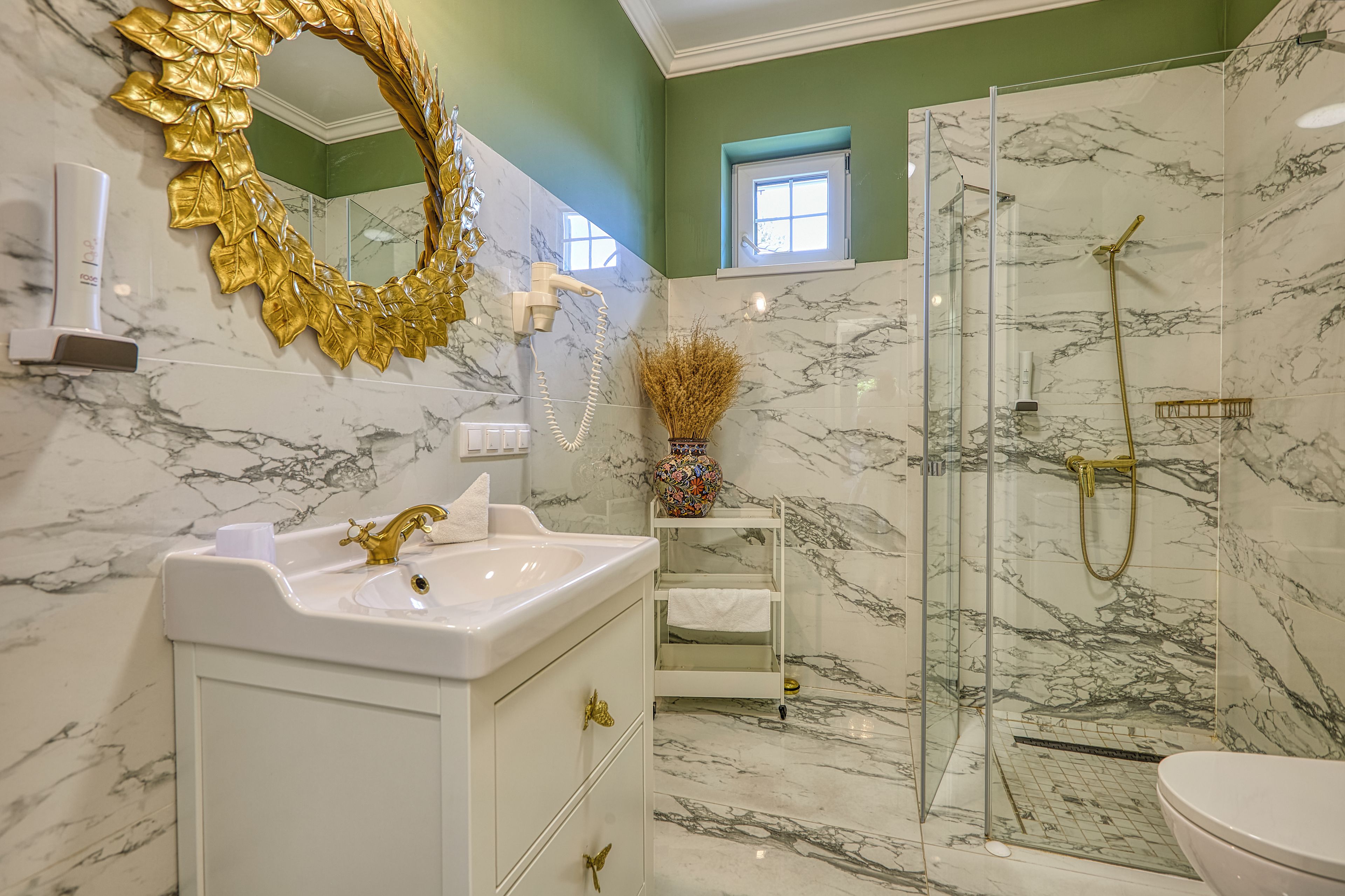 Un baño con cabina de ducha de mármol, espejo con pan de oro y lavamanos blanco.