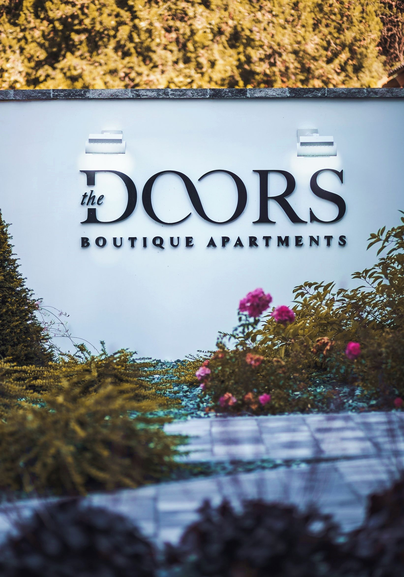 A sign for 'The Doors Boutique Apartments' with a clear view of the sign's text and a blurred background of greenery.