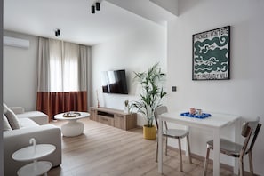 Een moderne woonkamer met een flatscreen televisie, een eethoek met een witte tafel en stoelen, en een grote kamerplant.