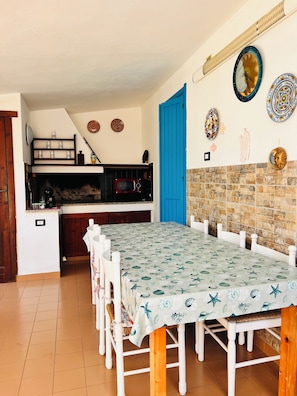 A dining area with a long table, chairs, a kitchen in the background, and decorative plates on the wall. - Cozy home just a 5-minute walk from the beach, along Geremeas Bay (Geremeas)