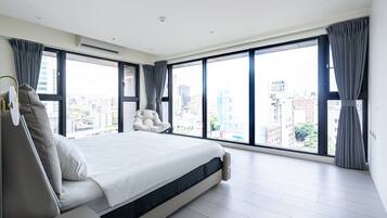A modern bedroom with a large bed, a chair, and a view of the city through floor-to-ceiling windows.