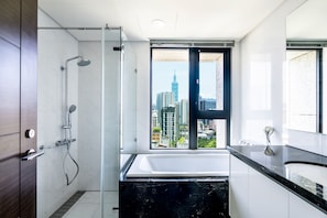 A modern bathroom with a shower, a bathtub, and a large window offering a city view.