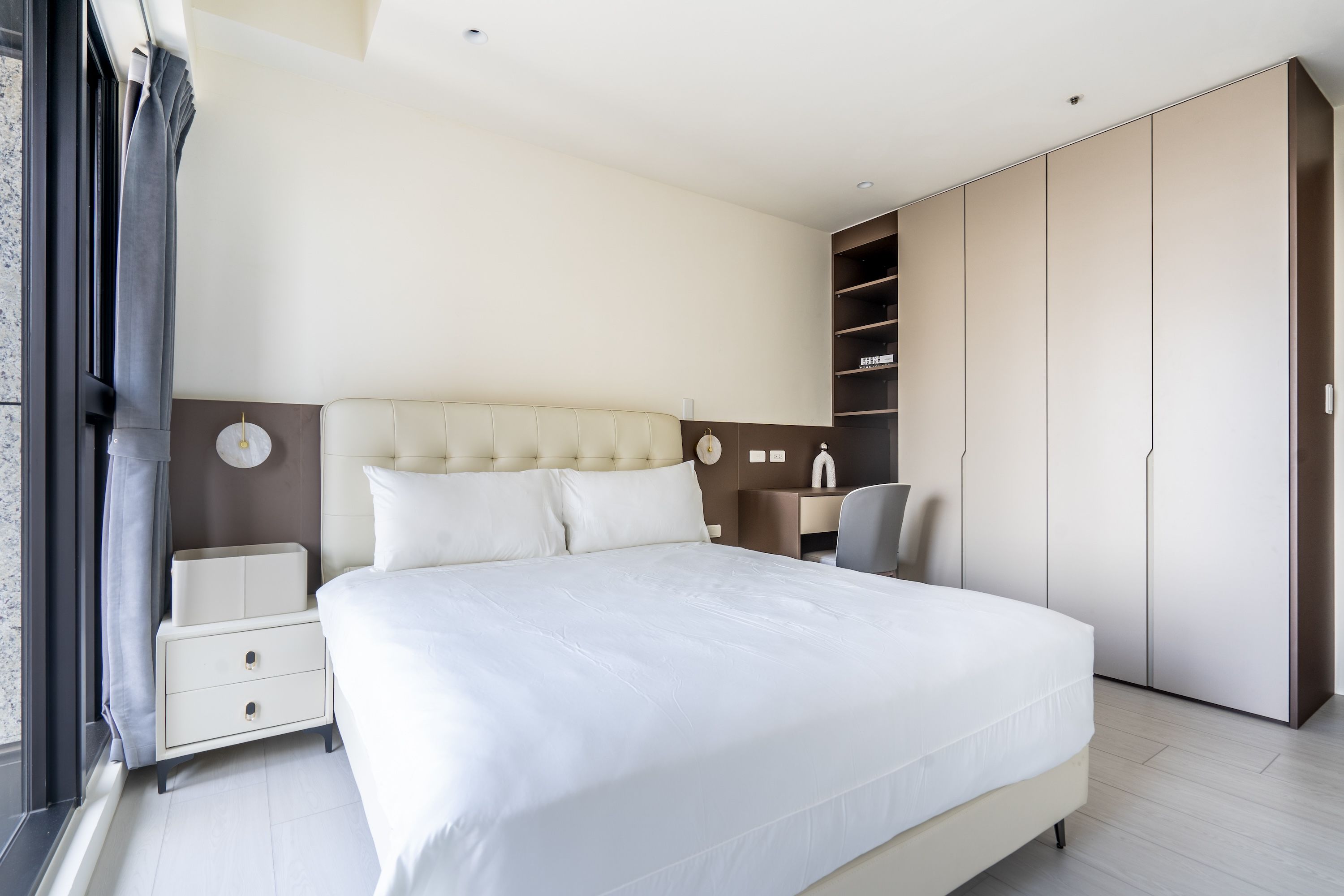 Una habitación de hotel moderna con una cama grande, una mesita de noche, una silla y un armario.