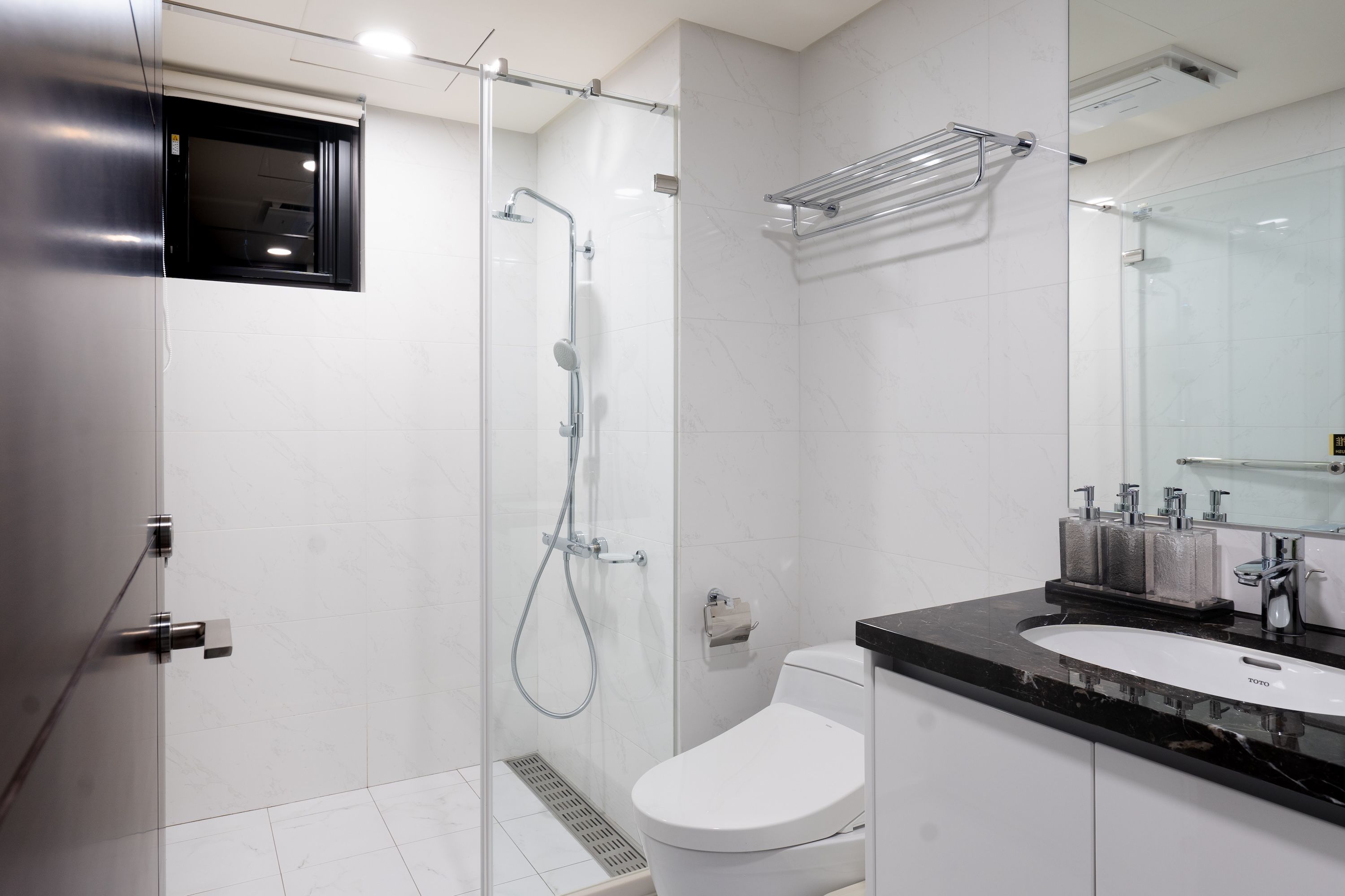Un baño moderno con ducha envuelta en vidrio, inodoro blanco y tocador negro con lavamanos y espejo.