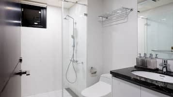 Un baño moderno con ducha envuelta en vidrio, inodoro blanco y tocador negro con lavamanos y espejo.