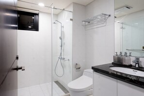 Un baño moderno con ducha envuelta en vidrio, inodoro blanco y tocador negro con lavamanos y espejo.