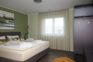 Een slaapkamer met een bed, een raam met gordijnen, een schilderij aan de muur en een kledingkast.