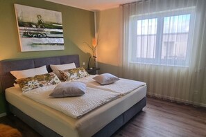Ein Schlafzimmer mit einem Bett, einem Bild an der Wand, einer Vase mit Blumen und einem Fenster mit Vorh ängen.